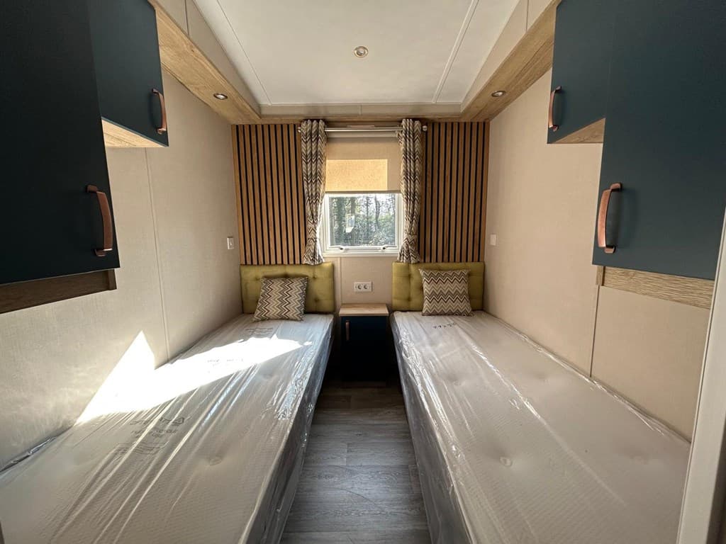 Tweepersoons slaapkamer met twee aparte bedden, kastruimtes en natuurlijk licht vanuit een raam.