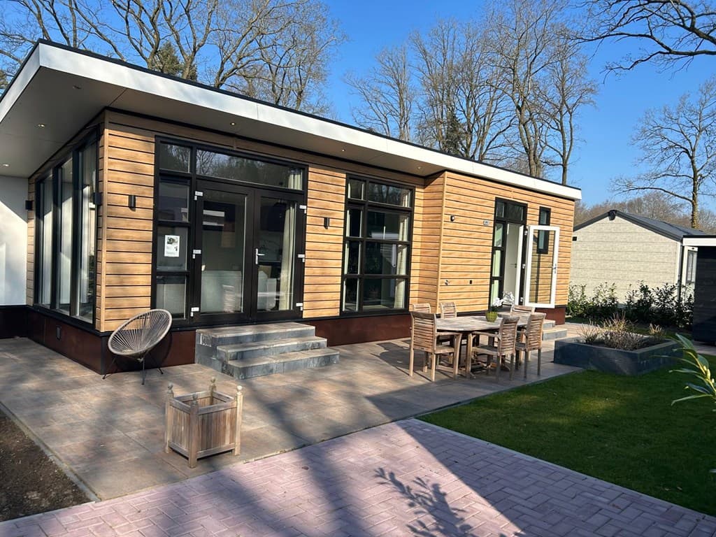 Moderne vakantiewoning met houten gevel, grote ramen en een terras met tuinmeubilair en groene ruimte rondom.