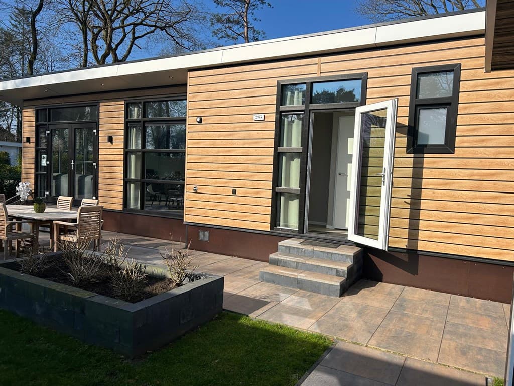 Moderne woning met houten gevel, terras met tuinmeubels en een opengeschoven voordeur in Harderwijk.