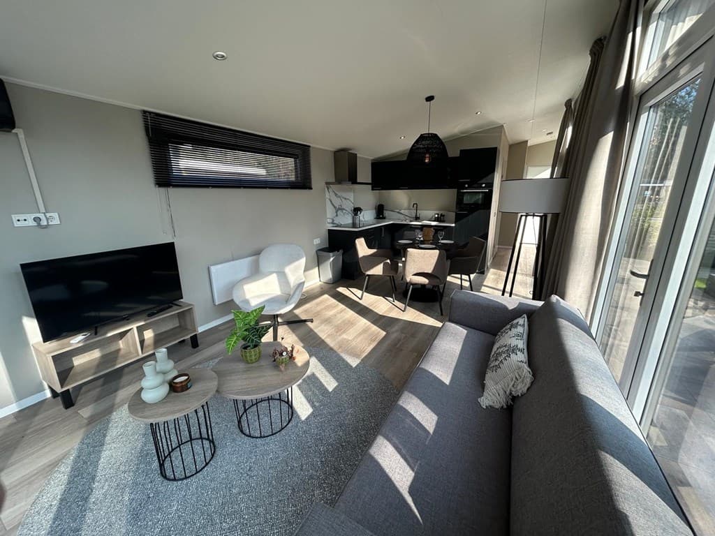 Lichte woonkamer met moderne meubels, een bank, eettafel en open keuken, grote ramen zorgen voor veel natuurlijk licht