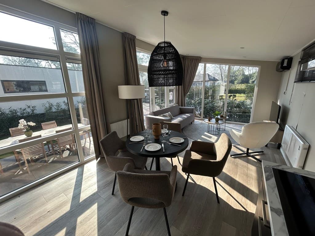 Gezellige eet- en woonruimte met een ronde tafel, comfortabele stoelen en veel natuurlijk licht van de ramen.