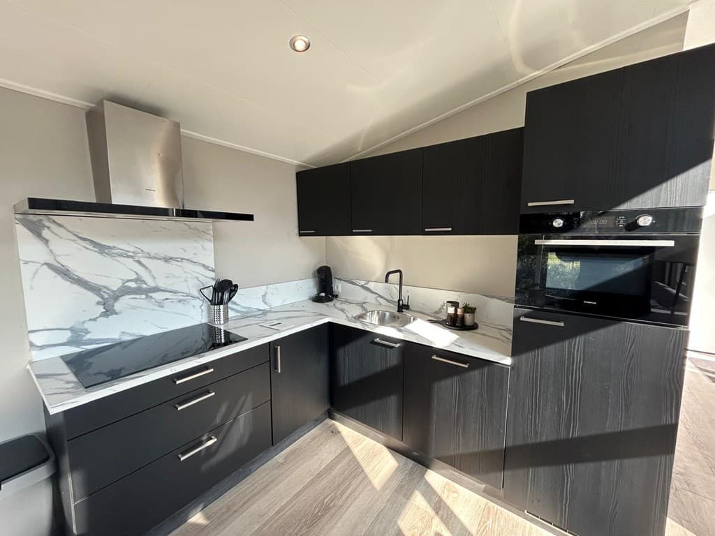 Moderne keuken met zwarte kasten, marmeren achterwand, inductiekookplaat en ingebouwde oven in lichte ruimte.