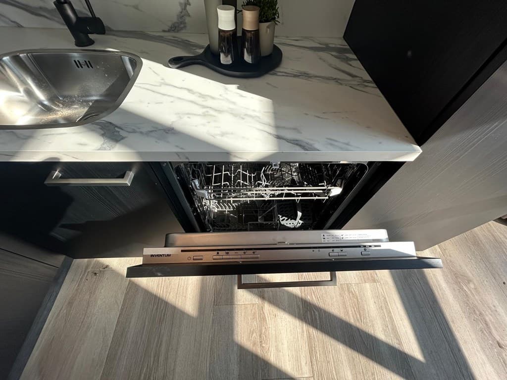 Afbeelding van een openvaatwasser in een moderne keuken met een marmeren werkblad en houten vloer