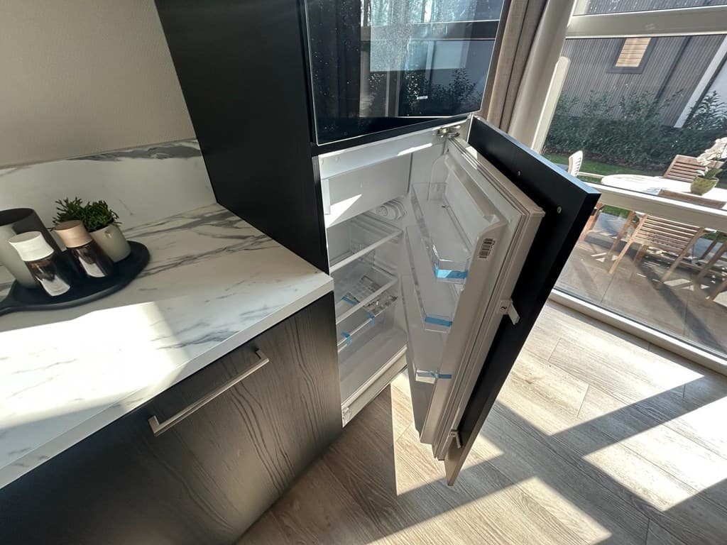 Keuken met open koelkast, marmeren aanrecht en uitzicht op een terras met zitmeubels buiten.