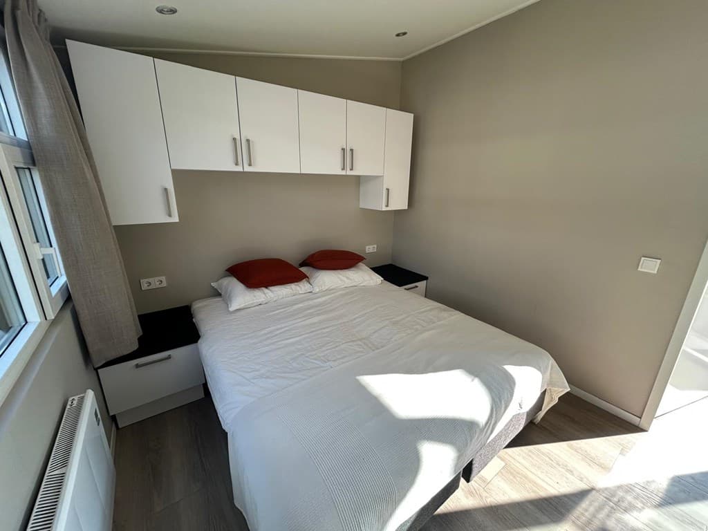 Slaapkamer met een bed, verlichting boven en wandkasten in neutrale kleuren.