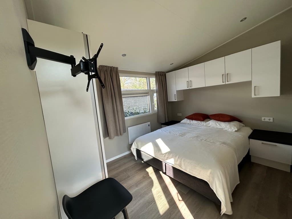 Slaapkamer met een tweepersoonsbed, muurkast en een televisiebeugel, voorzien van natuurlijk licht en neutrale kleuren