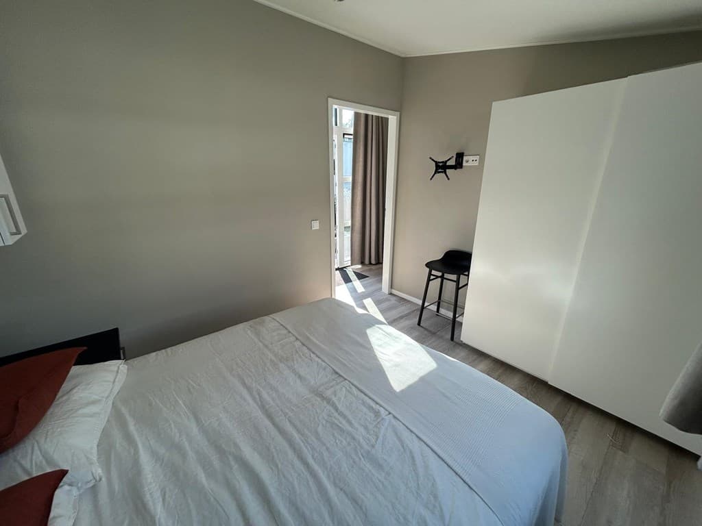 Hoek van een slaapkamer met een bed, kast en toegang tot een balkon met lichtinval.