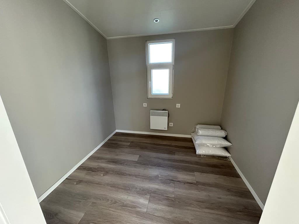 Lege kamer met twee ramen, een verwarmingselement en opgestapelde kussens op de vloer