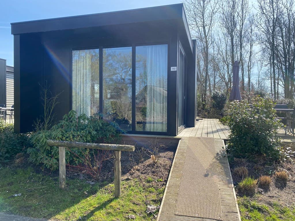 Moderne vakantiewoning met grote ramen, houten terras en groene borders bij Vakantiepark De Wiedense Meren.