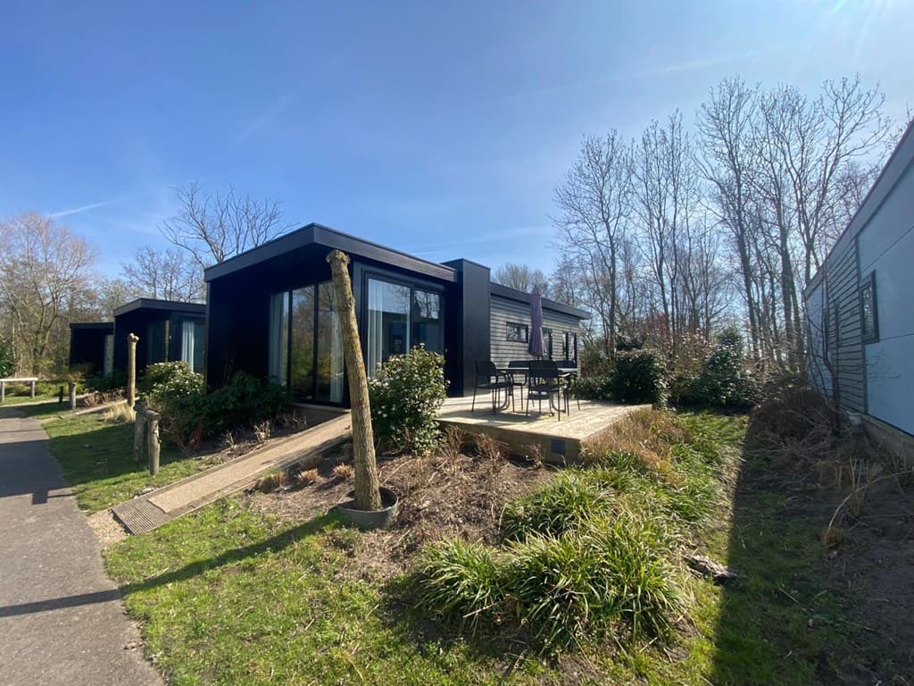 Moderne vakantiewoning met terras en tuinstoelen, omringd door bomen en groen in vakantiepark De Wiedense Meren.