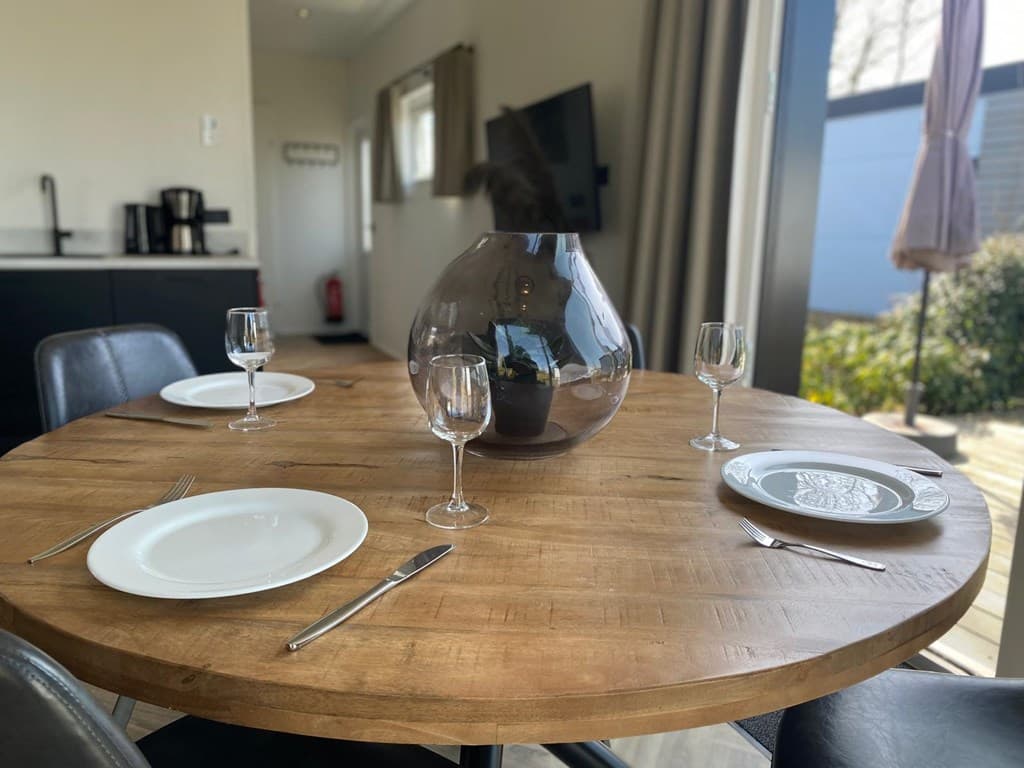 Eettafel met wijnglazen en servies, moderne keuken zichtbaar op de achtergrond, licht interieur met grote ramen