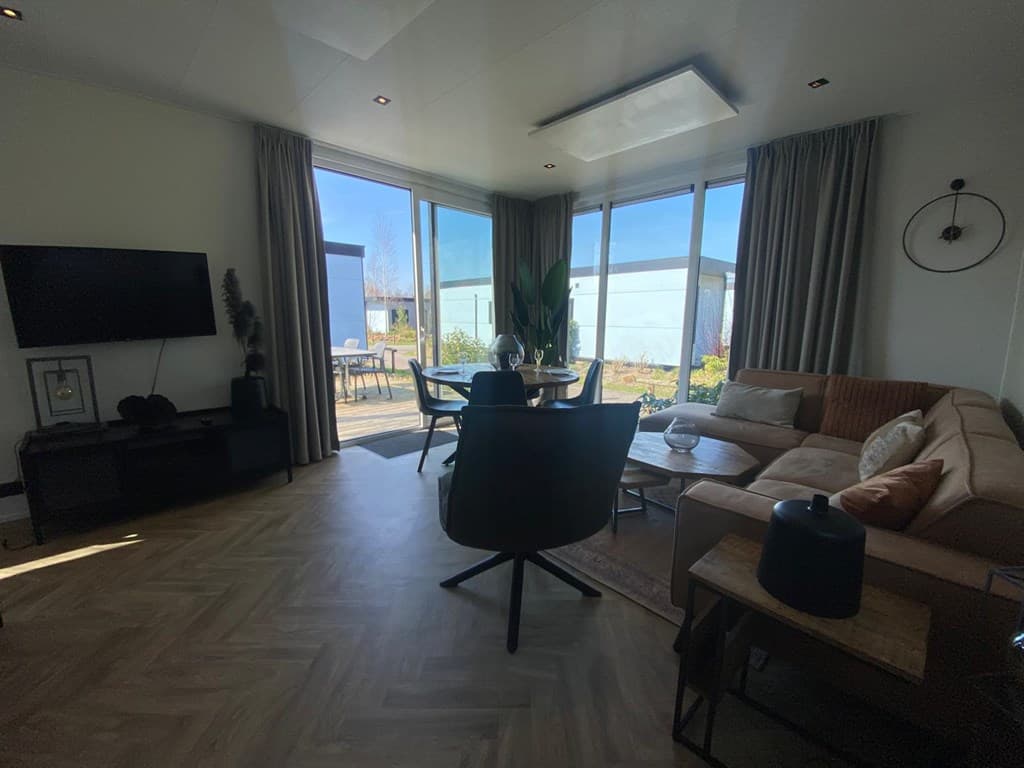 Lichte woonkamer met grote ramen, comfortabele bank, eettafel en uitzicht op buitenruimte bij vakantiepark De Wiedense Meren.