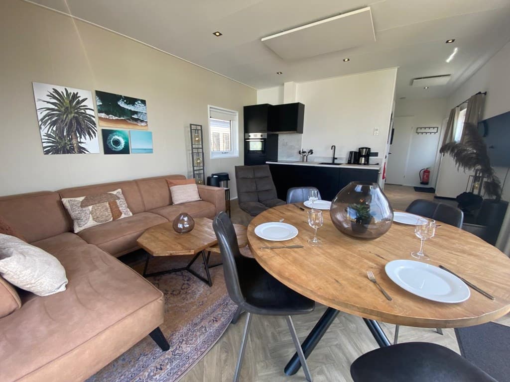 Ingerichte woonkamer met bank, eetkamertafel en open keuken in een vakantiewoning op een vakantiepark.
