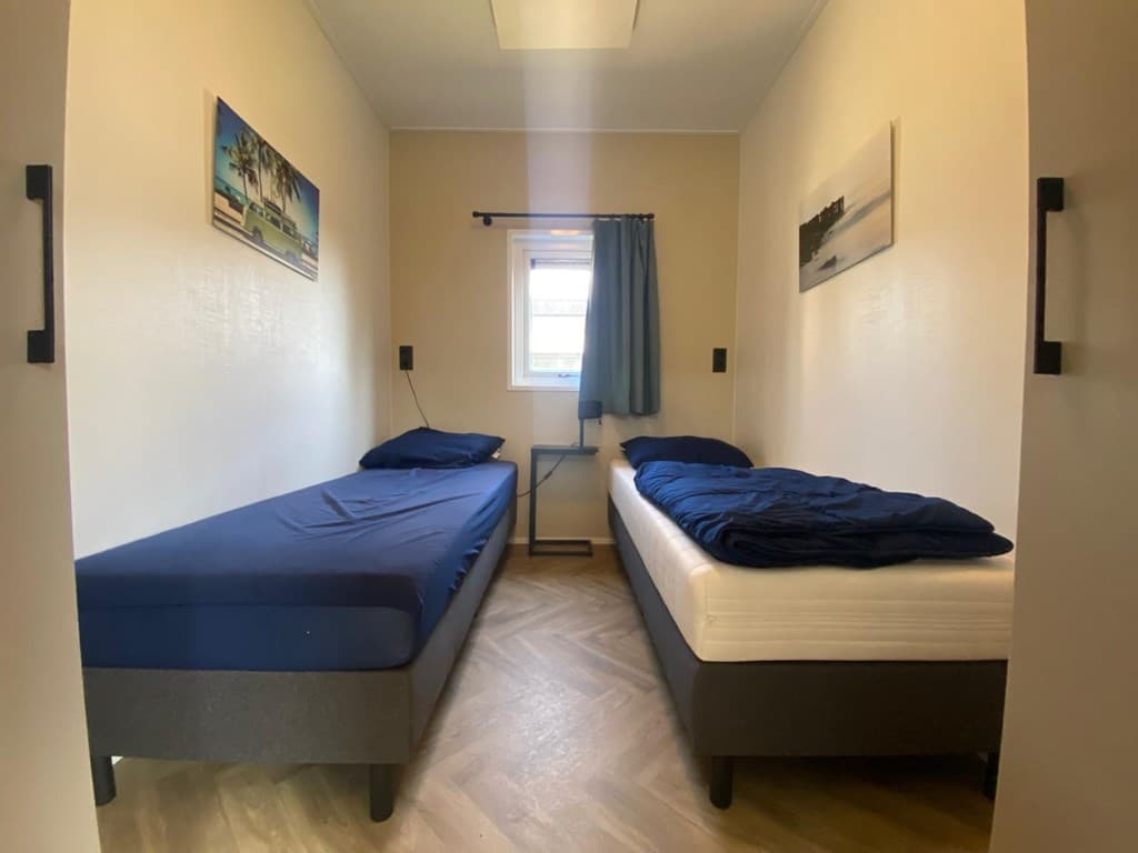Slaapkamer met twee eenpersoonsbedden, raam met blauwe gordijnen en houten vloer.