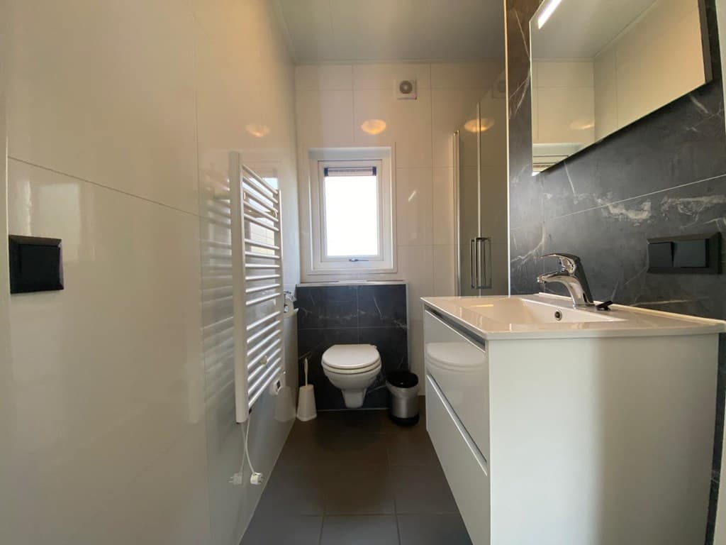 Moderne badkamer met witte tegels, verwarmingsradiator, inloopdouche en wastafel met spiegel.