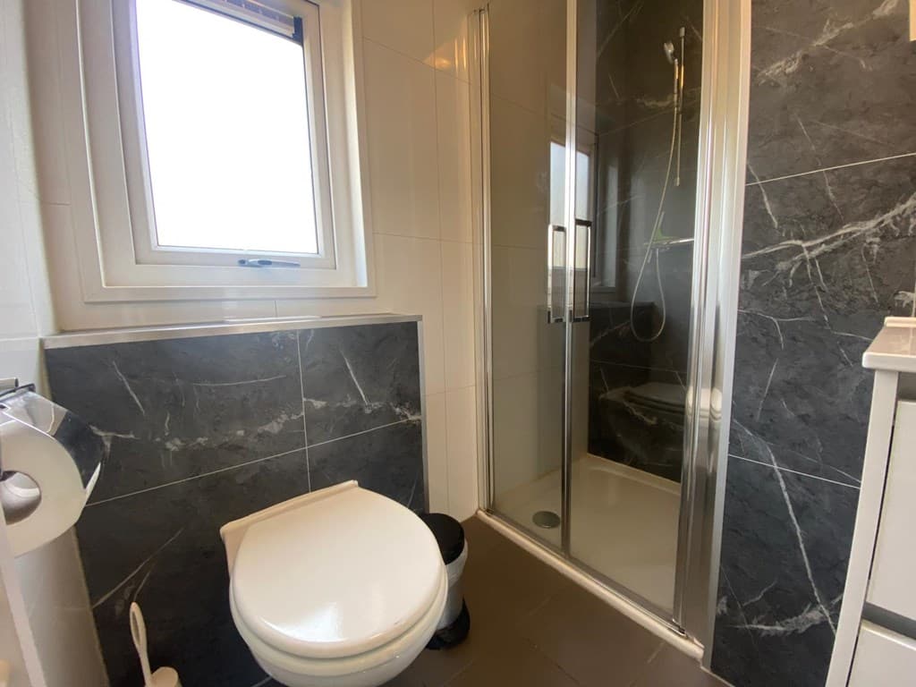 Badkamer met douchecabine, toilet en raam met uitzicht op buiten, betegelde wanden en vloeren.