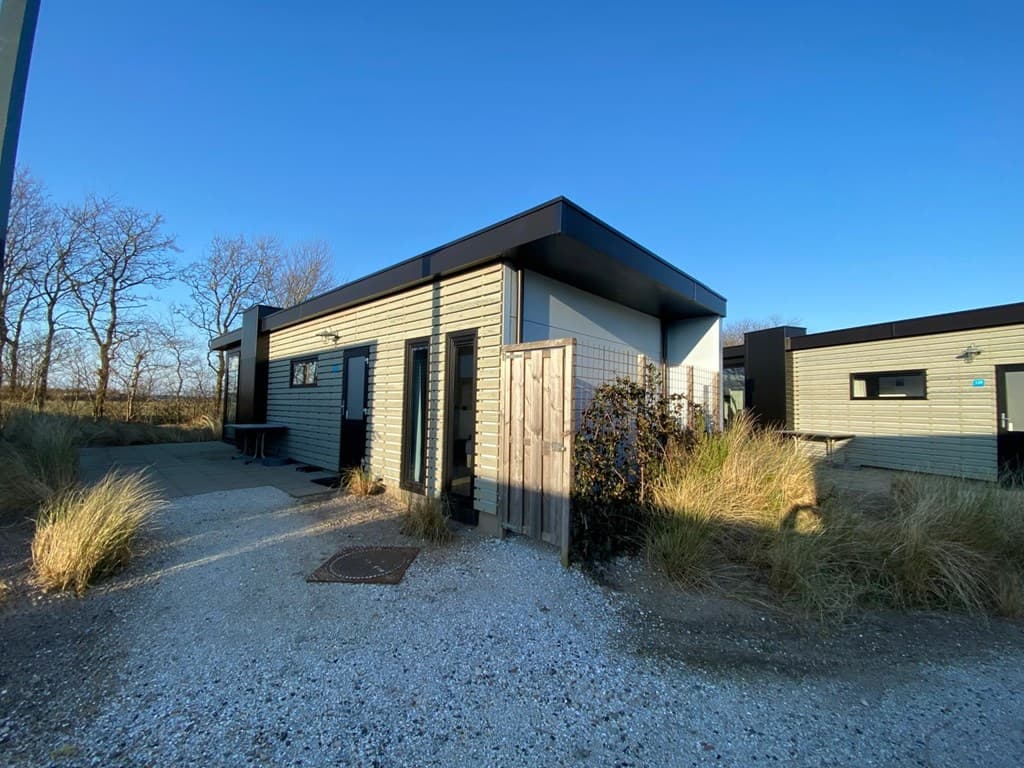 Moderne vakantiewoning met een houten gevel, omgeven door gras en een houten schutting, gelegen in een rustige omgeving