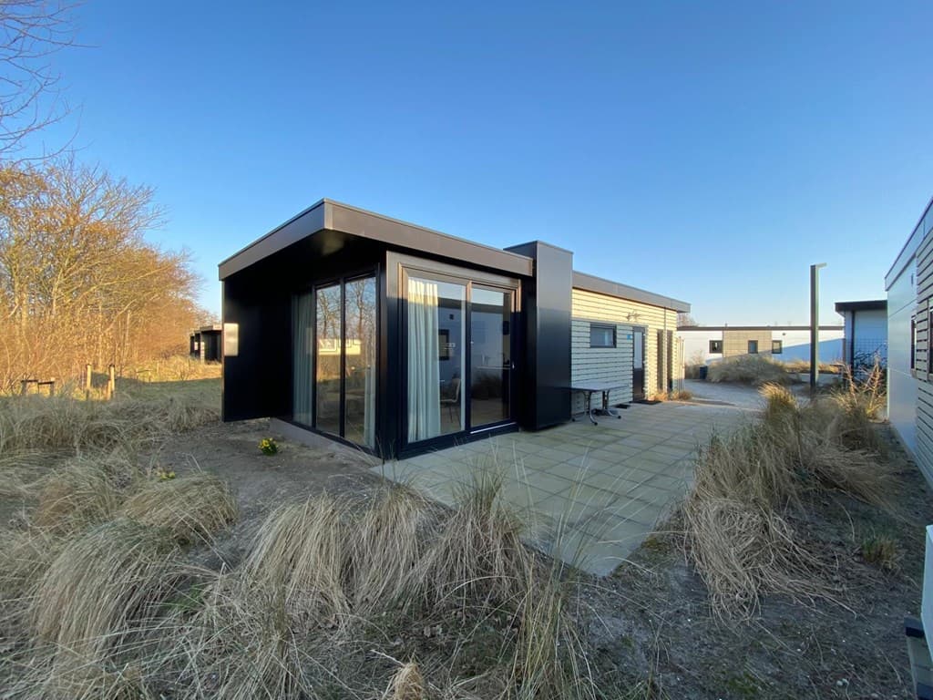 Moderne vakantiewoning met glazen gevel en terras, omgeven door gras en natuurelementen in EuroParcs Texel.