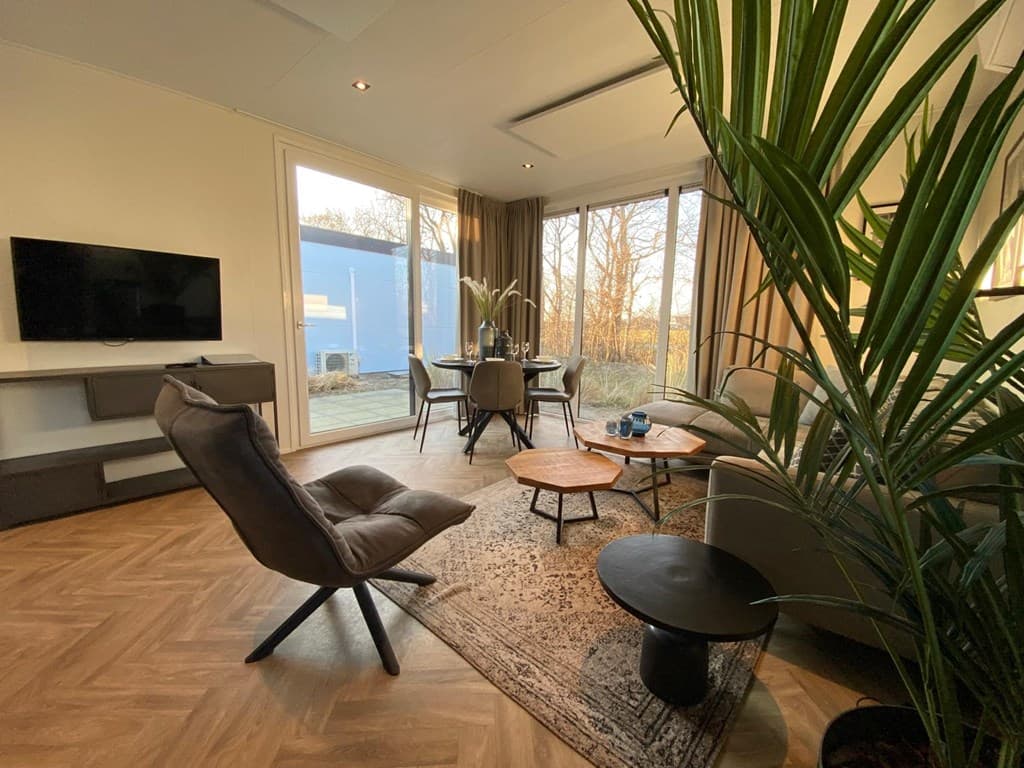 Moderne woonkamer met zithoek, eettafel en grote ramen met uitzicht op buitenruimte en groen.