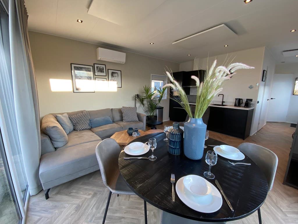 Moderne woonkamer met zithoek, eettafel en keuken, lichte kleuren en decoratieve planten op tafel.