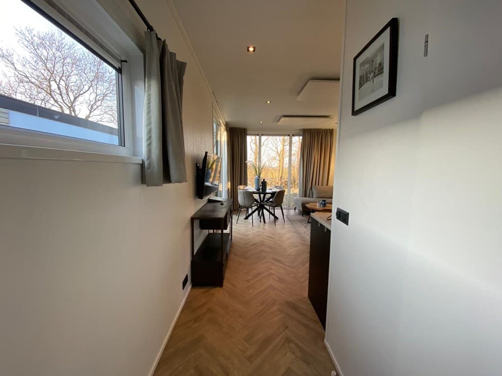 Ingang naar een moderne woning met een woonkamer, een eetgedeelte en grote ramen voor natuurlijk licht.