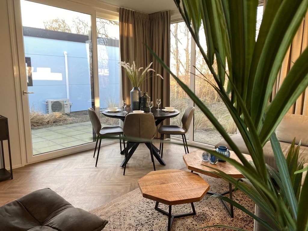 Eethoek met ronde tafel en stoelen, grote ramen met uitzicht op buiten, planten en woondecoratie zichtbaar.