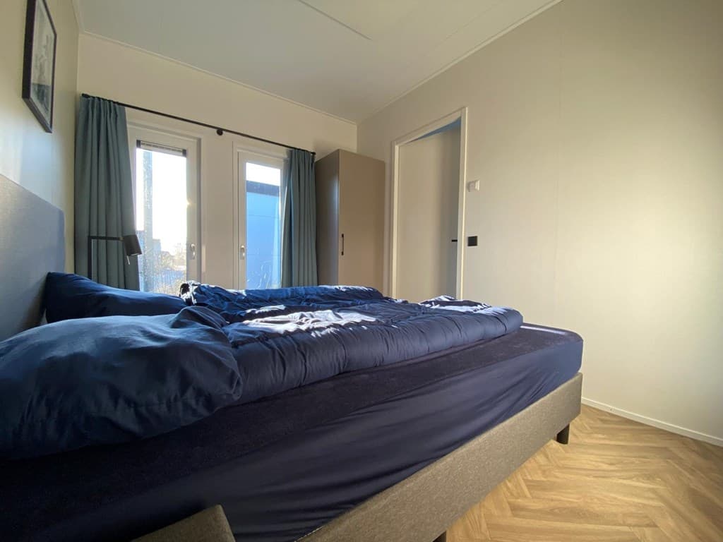 Slaapkamer met een tweepersoonsbed, lichtgekleurde muren en toegang tot een terras via openslaande deuren.