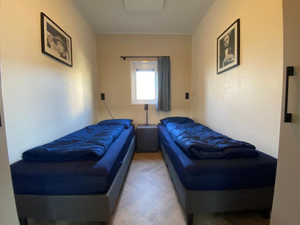 Slaapkamer met twee eenpersoonsbedden en een raam, kunst aan de muur en een nachtkastje tussen de bedden