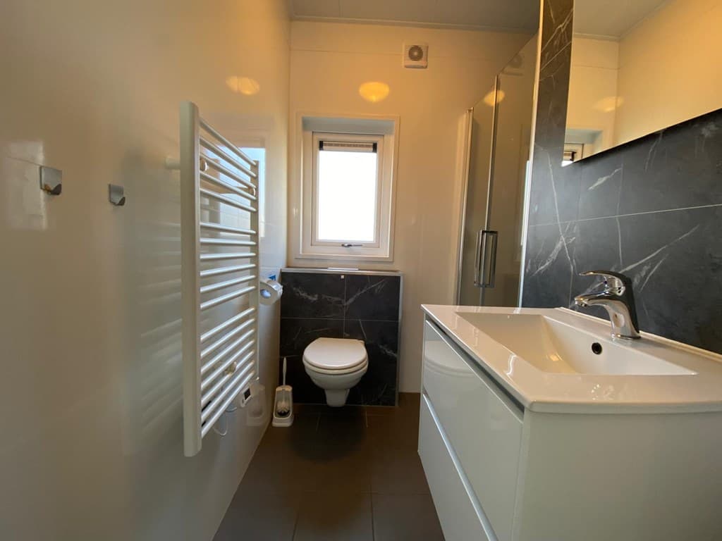 Moderne badkamer met wastafel, toilet, handdoekenradiator en douchescherm in lichte en donkere kleuren