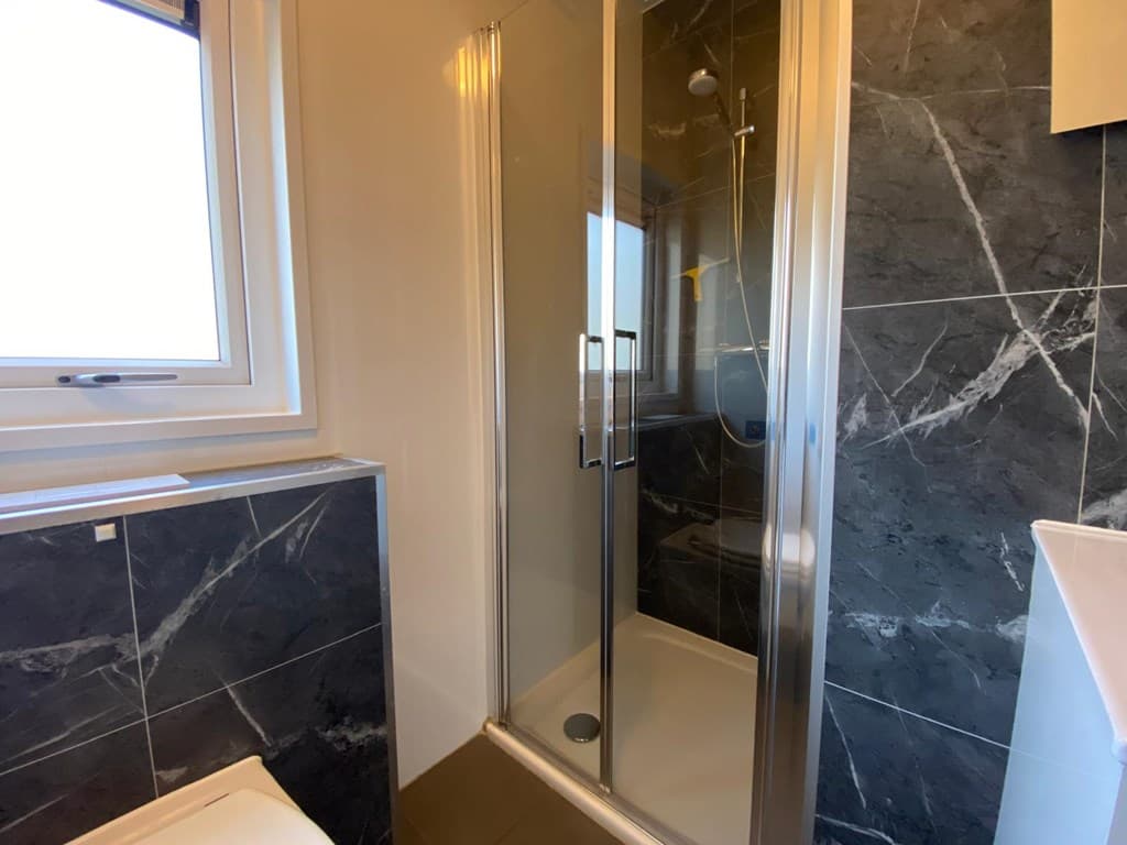 Moderne badkamer met inloopdouche, tegelwanden en venster voor natuurlijk licht.