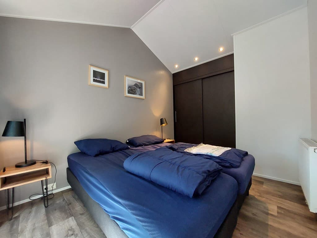 Slaapkamer met een tweepersoonsbed, nachtkastjes, wandlampen en een inbouwkast tegen een grijze wand