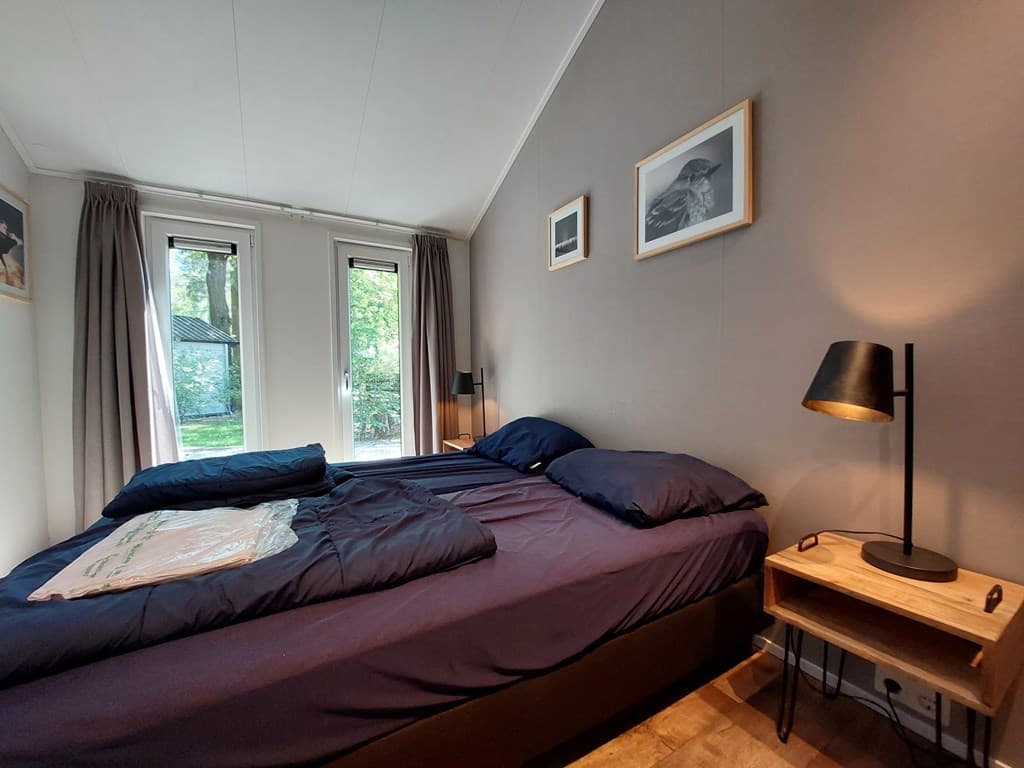Slaapkamer met twee eenpersoonsbedden, een nachtkastje en grote ramen met uitzicht op groen.