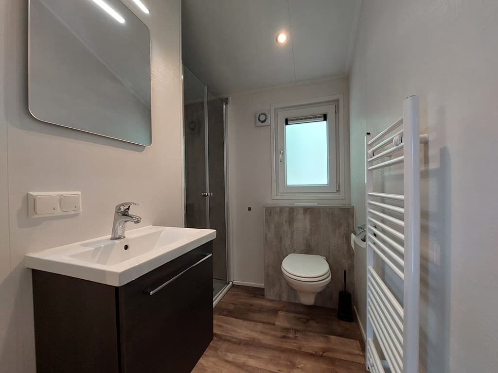 Moderne badkamer met wastafel, douchecabine, toilet en handdoekenradiator in een lichte ruimte