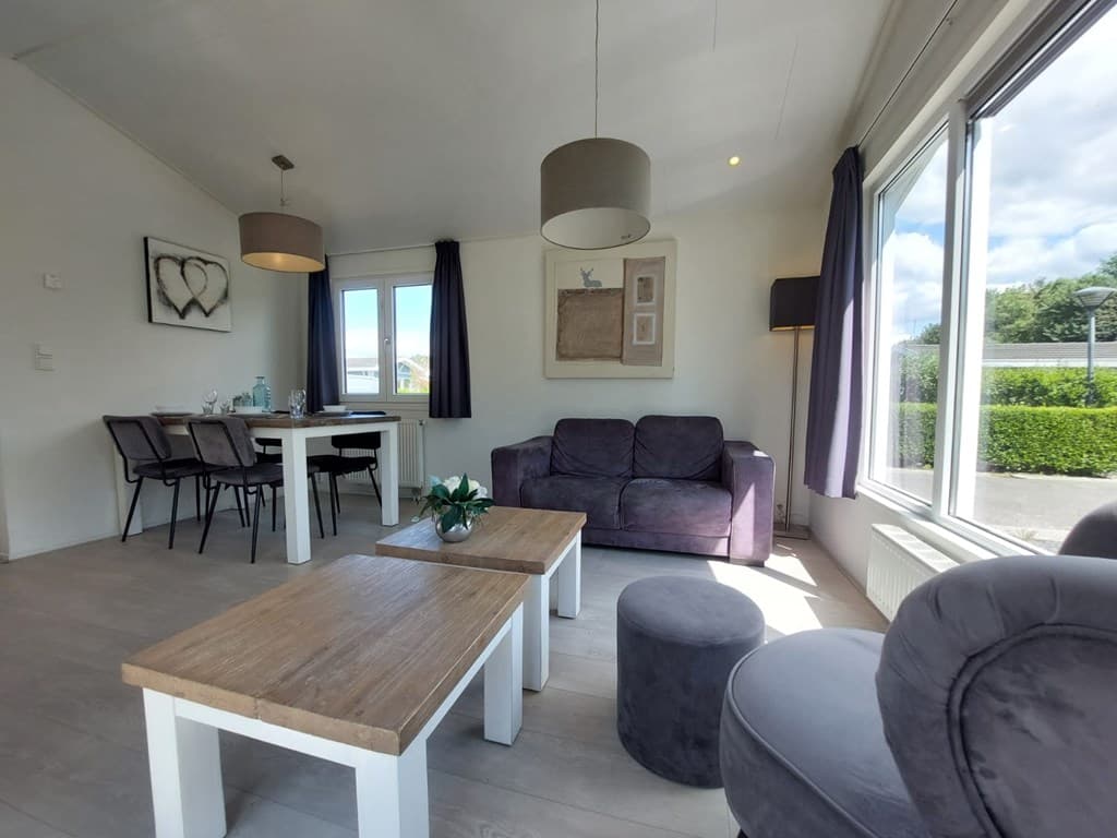 Lichte woonkamer met zithoek, eettafel en uitzicht op de buitenruimte met groene haag.