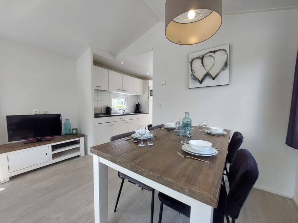 Eettafel met vier stoelen, televisie en keuken in lichte woonkamer met schilderij aan de muur