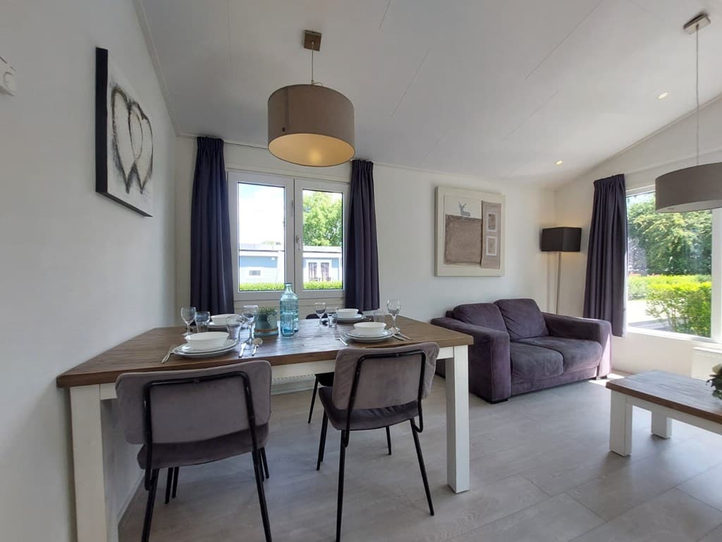 Eet- en woonkamer met een tafel, stoelen, bank en raam met uitzicht op groen buiten.