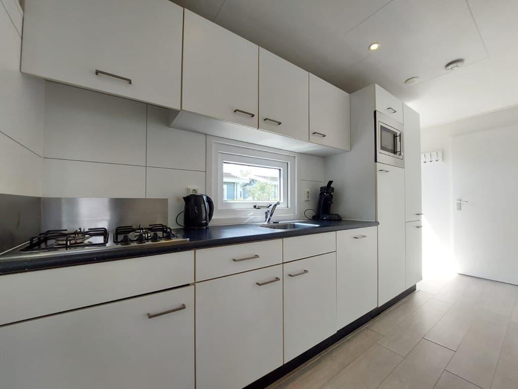Moderne keuken met witte kasten, ingebouwde apparaten en afgewerkt met een zwart aanrechtblad, veel lichtinval.