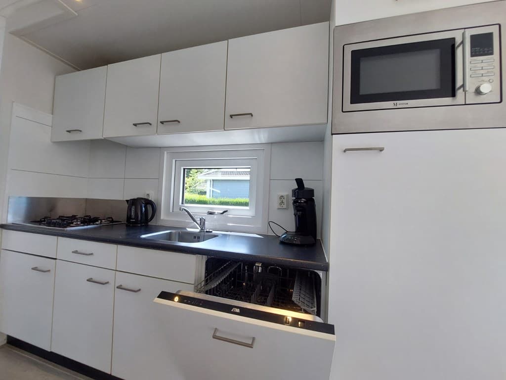 Moderne keuken met ingebouwde apparatuur, waaronder een vaatwasser, magnetron en kookplaat, met uitzicht op de buitenruimte.