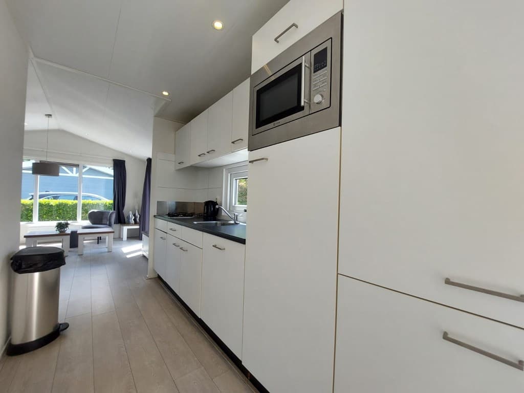Moderne keuken met witte kasten, aanrecht en ingebouwde apparaten, uitzicht op woonkamer met zitgedeelte en natuurlijk licht