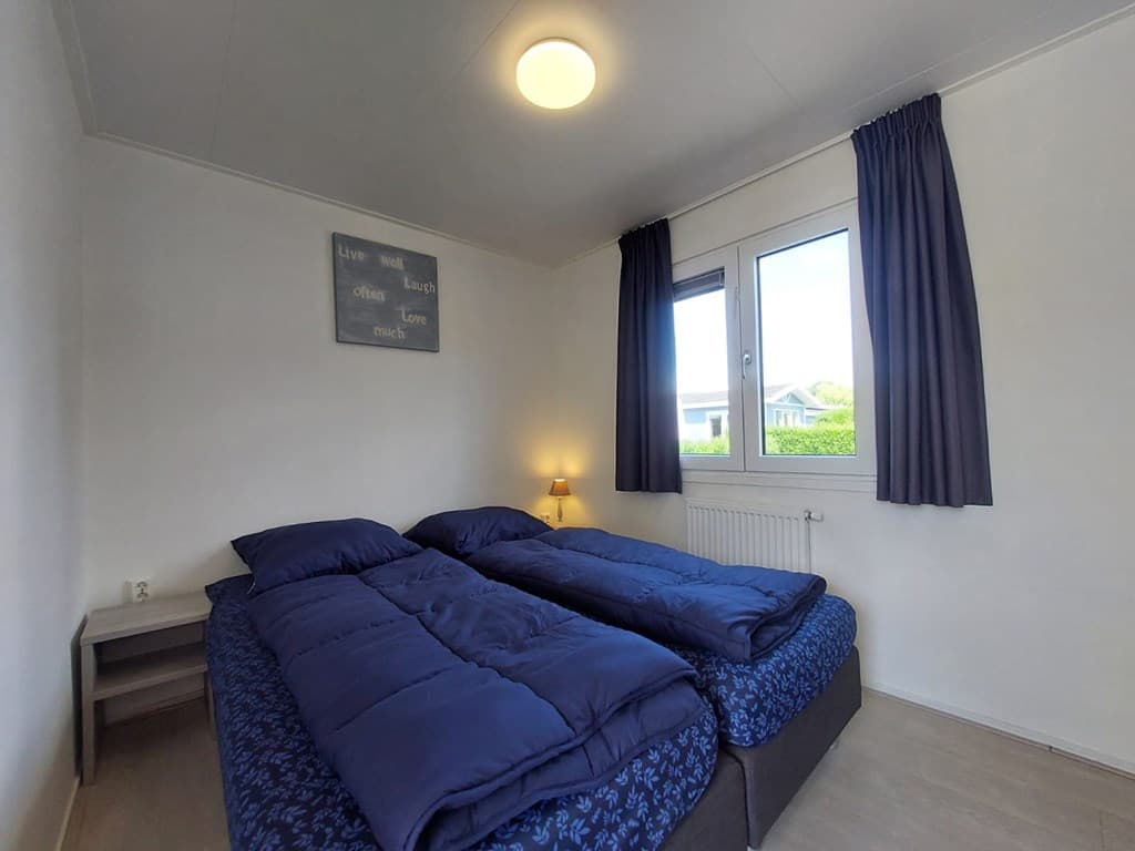 Slaapkamer met twee aparte bedden, een nachtkastje, raam met uitzicht en gordijnen