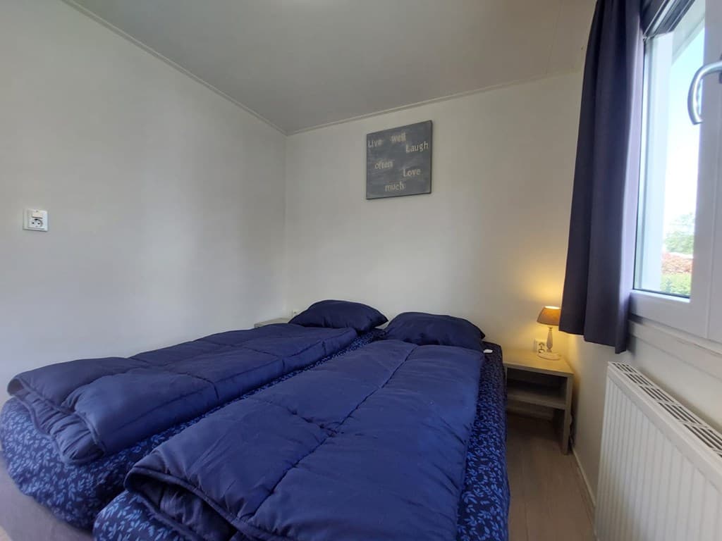 Slaapkamer met twee eenpersoonsbedden en een nachtkastje met lamp, raam met zicht naar buiten.
