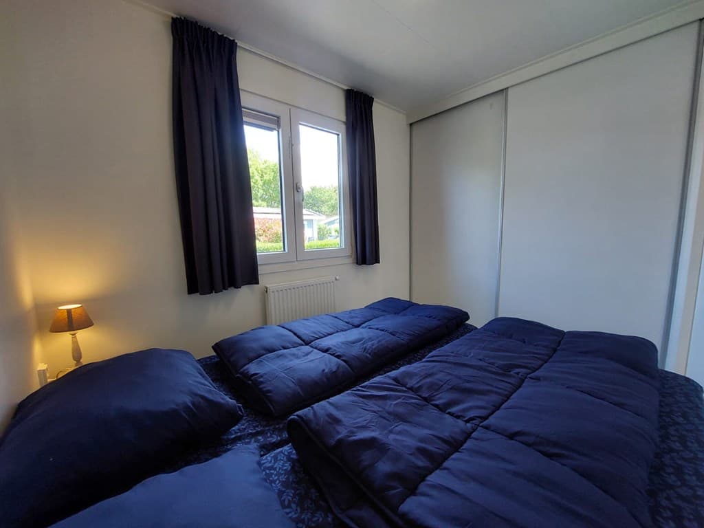 Slaapkamer met twee losse bedden en raam met uitzicht op de buitenruimte, verduisterende gordijnen en een nachtlampje.