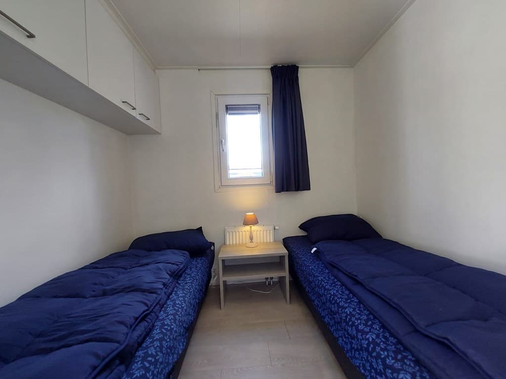 Slaapkamer met twee eenpersoonsbedden, een nachtkastje en een raam met een gordijn