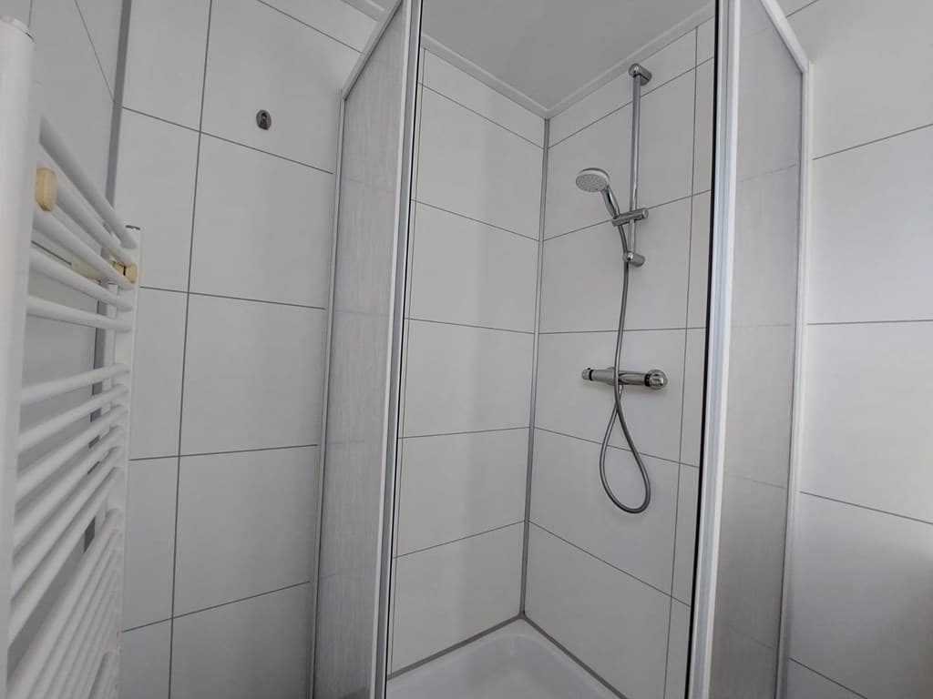 Douchecabine met glazen wanden, groene douchekop en een handdoekenrek aan de muur