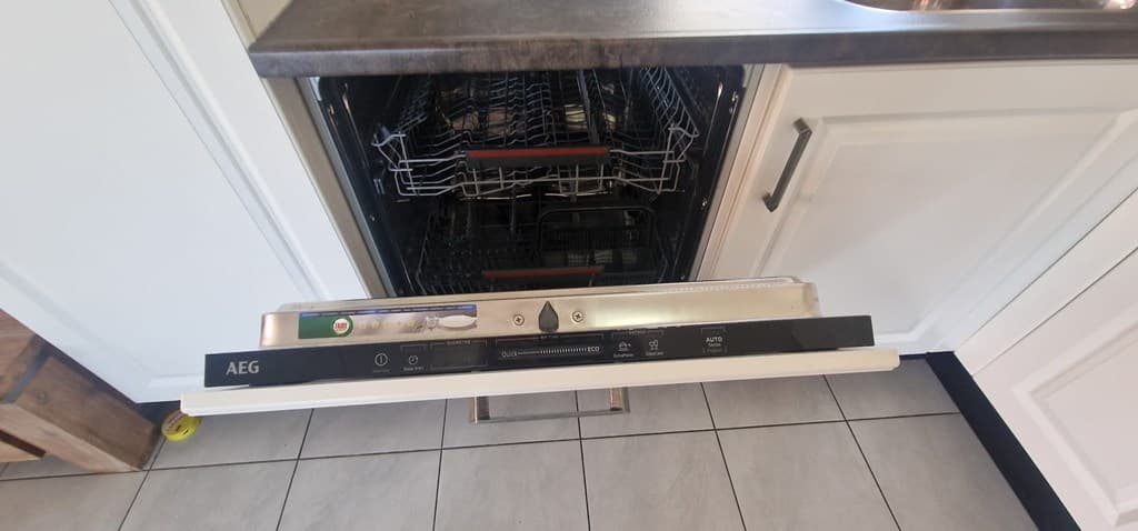 Een inbouwvaatwasser van AEG met open deurruimte in een moderne keuken met grijze tegels en witte kastjes