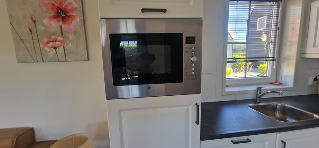 Keuken met een inbouwmagnetron en een spoelbak bij een raam met uitzicht op de tuin en een schilderij aan de muur.
