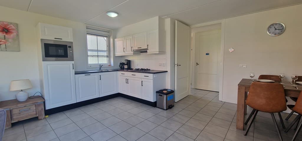 Moderne keuken met tafel en stoelen, lichte tegels en veel natuurlijke lichtinval.