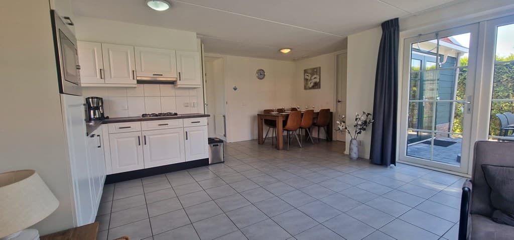 Moderne woonkamer met open keuken, eettafel voor zes personen en toegang tot de tuin via glazen deuren.