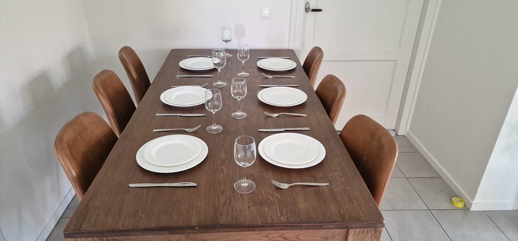 Eettafel met zes stoelen, gedekt met borden en glazen in een lichte, moderne omgeving.