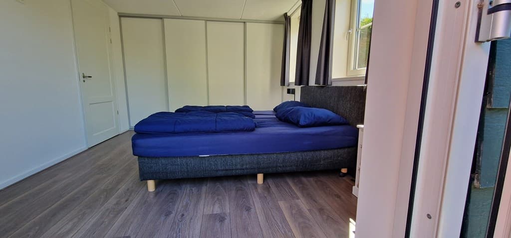 Slaapkamer met een tweepersoonsbed en twee raampjes, houten vloer en lichte muren